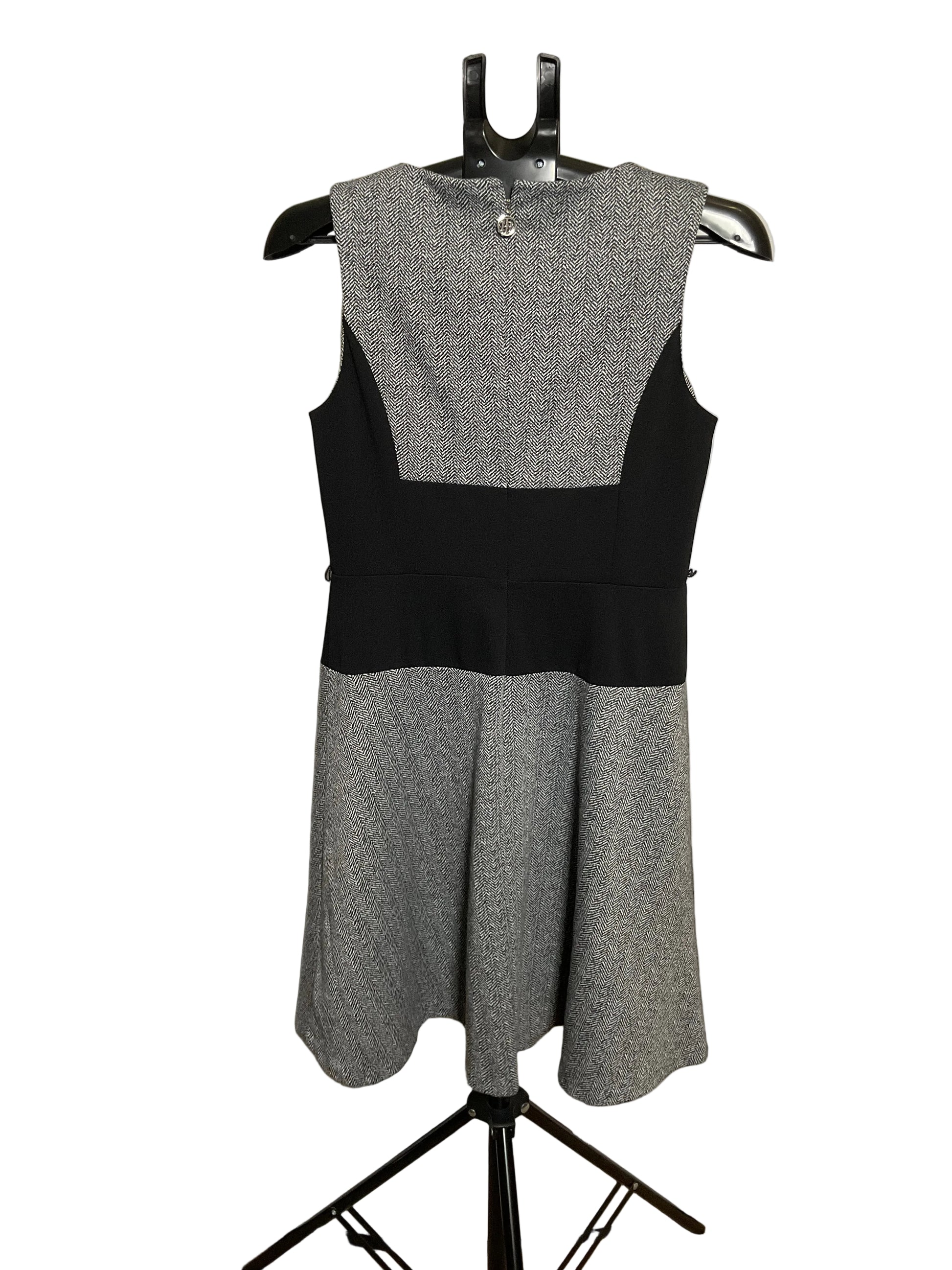 A sleeveless color-block dress displayed on a black hanger stand against a white circular studio backdrop. The dress has a heather gray upper yoke and flared skirt, with solid black side panels and a black waistband.