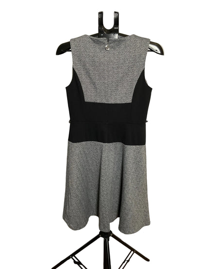 A sleeveless color-block dress displayed on a black hanger stand against a white circular studio backdrop. The dress has a heather gray upper yoke and flared skirt, with solid black side panels and a black waistband.