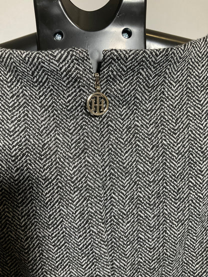 Close-up of a gray and white herringbone tweed fabric with a small circular metal logo charm featuring the letters 'HH'.