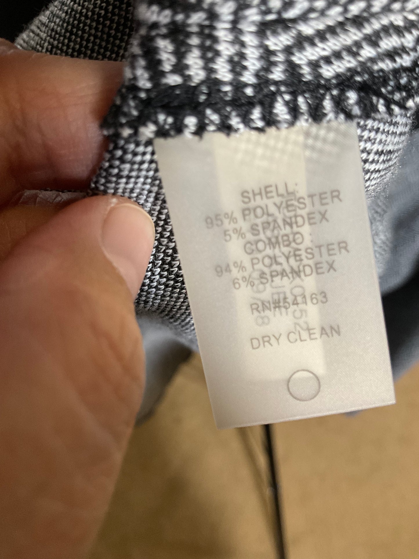 A close-up of a hand holding a garment label attached to black-and-white patterned fabric, with the text showing material composition: 95% polyester, 5% spandex.