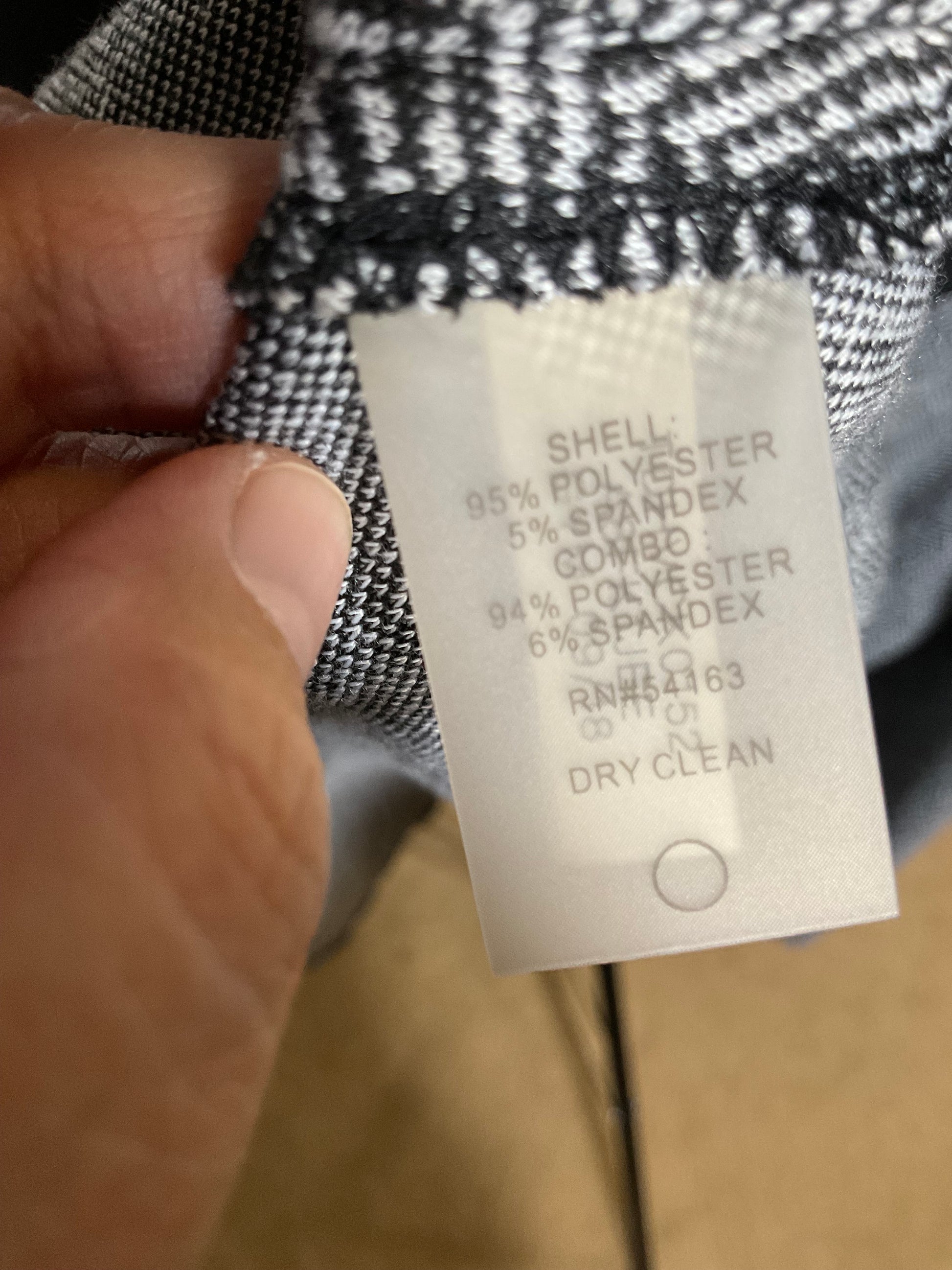A close-up of a hand holding a garment label attached to black-and-white patterned fabric, with the text showing material composition: 95% polyester, 5% spandex.