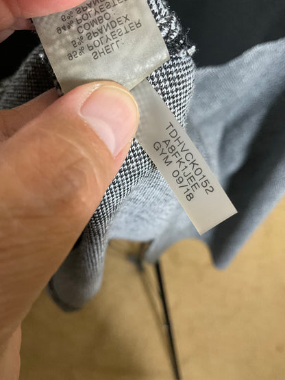A close-up of a hand holding the inner neck label of a gray and black houndstooth or micro-check garment, showing the size and garment code information.