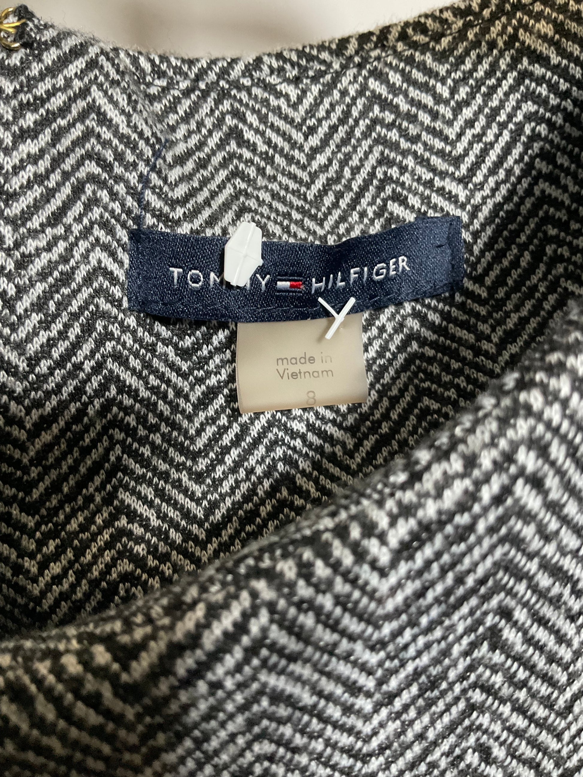 Close-up of a Tommy Hilfiger garment neck label on a black and white herringbone patterned fabric.