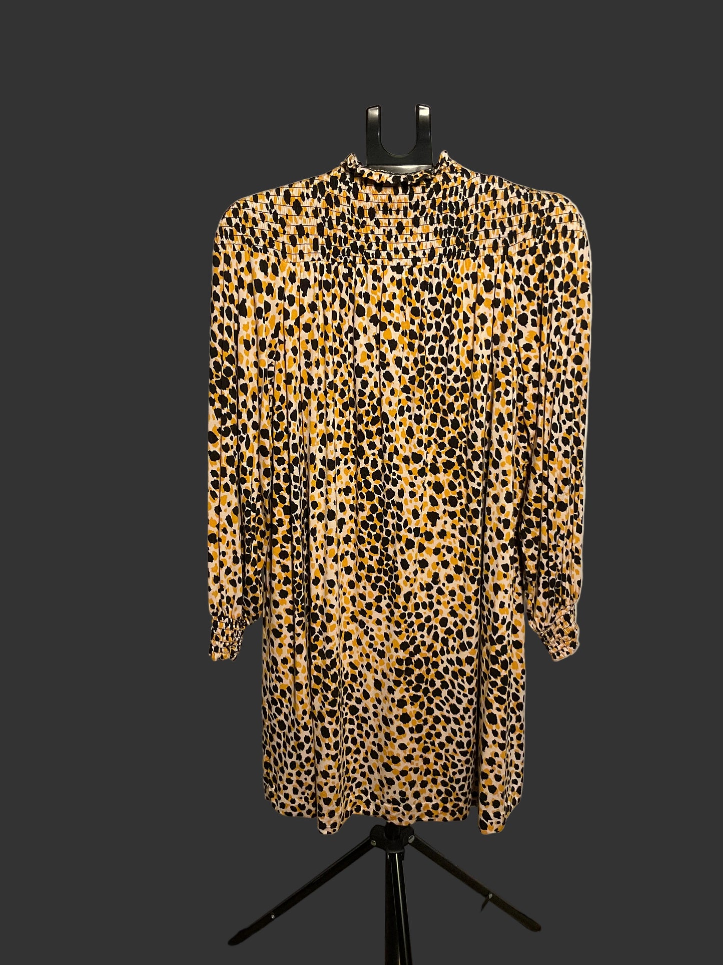 A leopard print long-sleeve dress displayed on a black hanger stand in front of a large white circular backdrop.