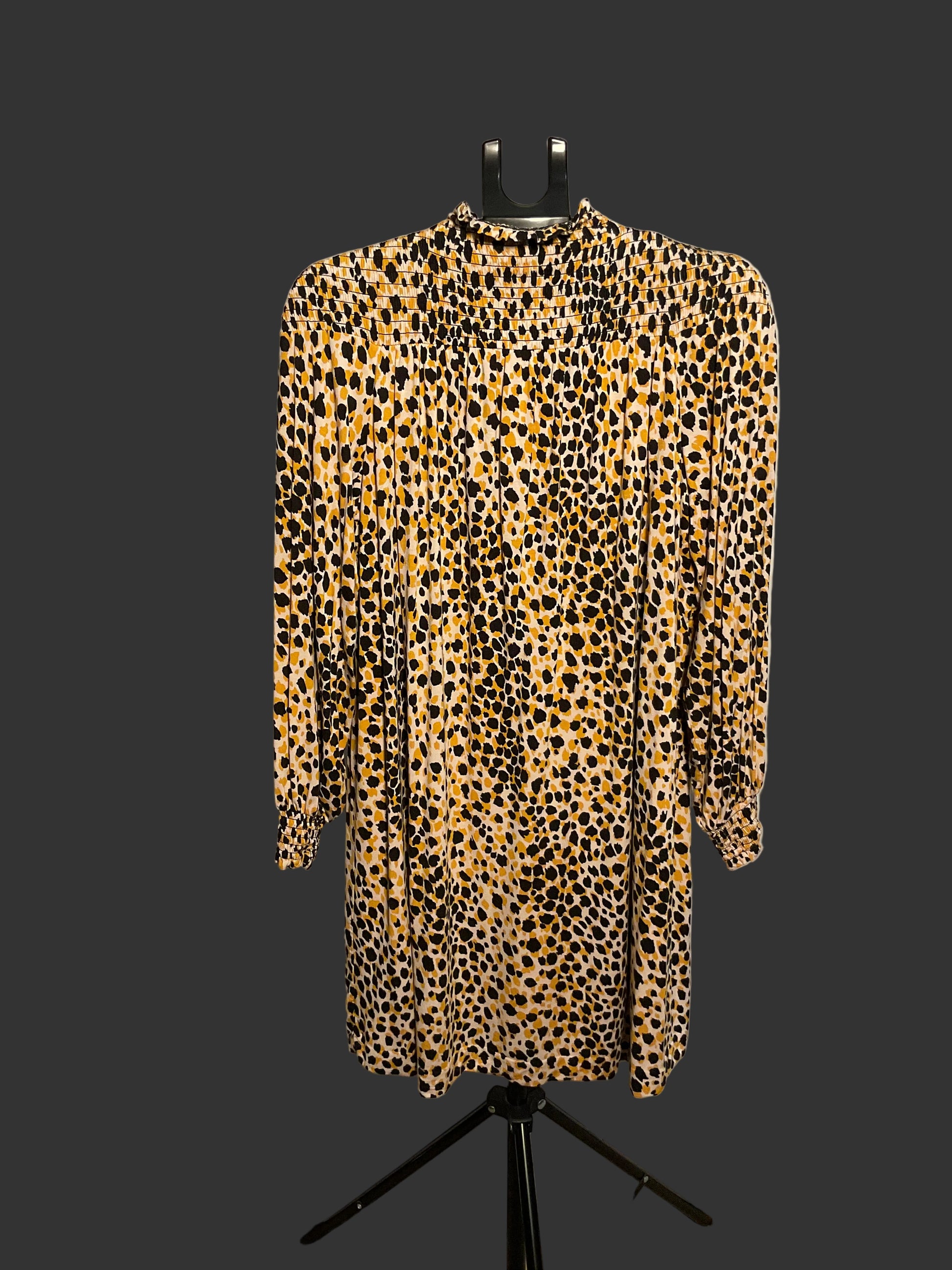 A leopard print long-sleeve dress displayed on a black hanger stand in front of a large white circular backdrop.