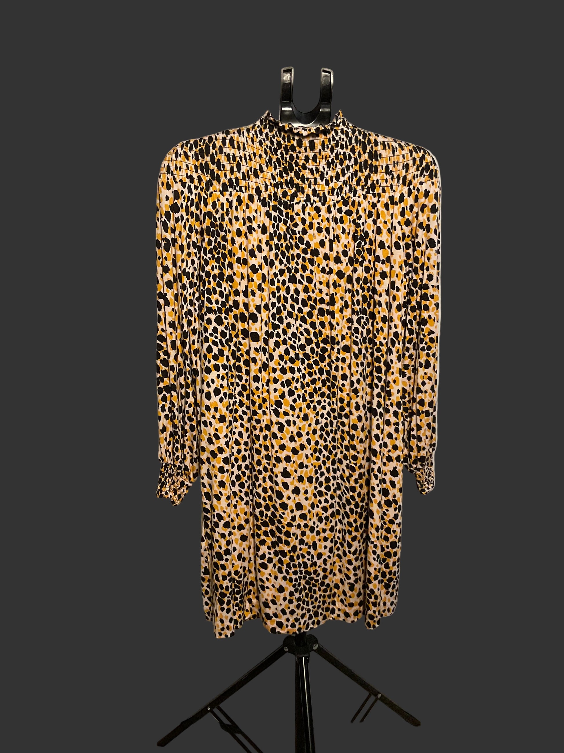 A leopard print long-sleeve shirt dress displayed on a black hanger stand in front of a white circular backdrop.