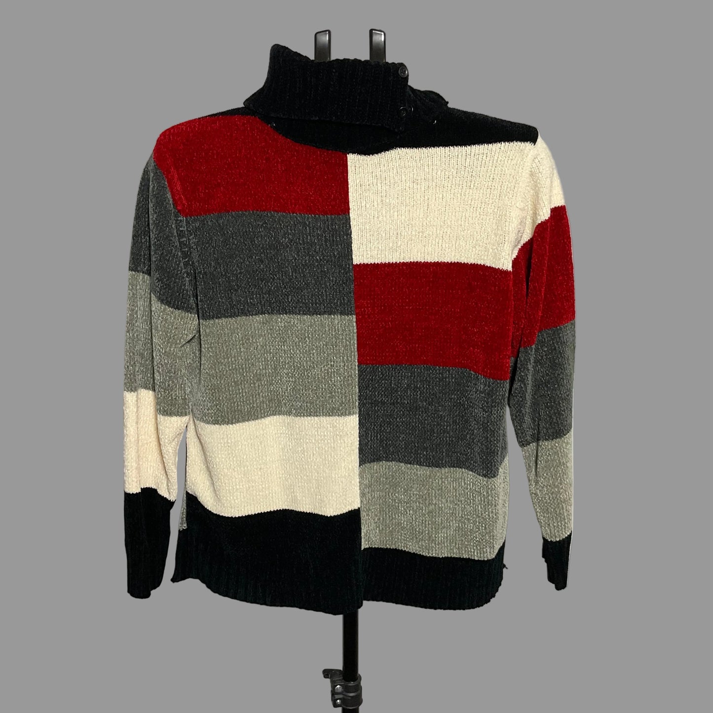 A knit turtleneck sweater with wide horizontal color-block stripes in red, cream, gray, and black, displayed on a black dress form against a plain light gray wall.