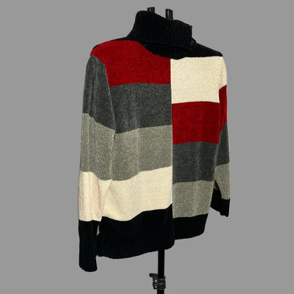 A knit turtleneck sweater with a large block pattern in red, cream, gray, and black, displayed on a black mannequin torso against a plain light gray wall.