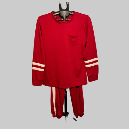 A red two-piece tracksuit set consisting of a long-sleeve shirt and matching pants, displayed on a hanger stand in front of a circular studio backdrop. The shirt features a chest pocket and white stripes on the sleeves, while the matching pants have white stripes down the side.