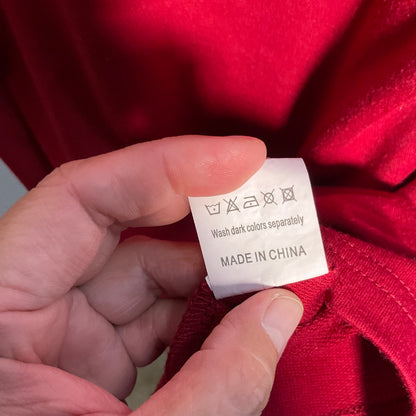 A close-up of a hand holding a white care label sewn onto a bright red garment, showing the text 'Wash dark colors separately' and 'MADE IN CHINA'.