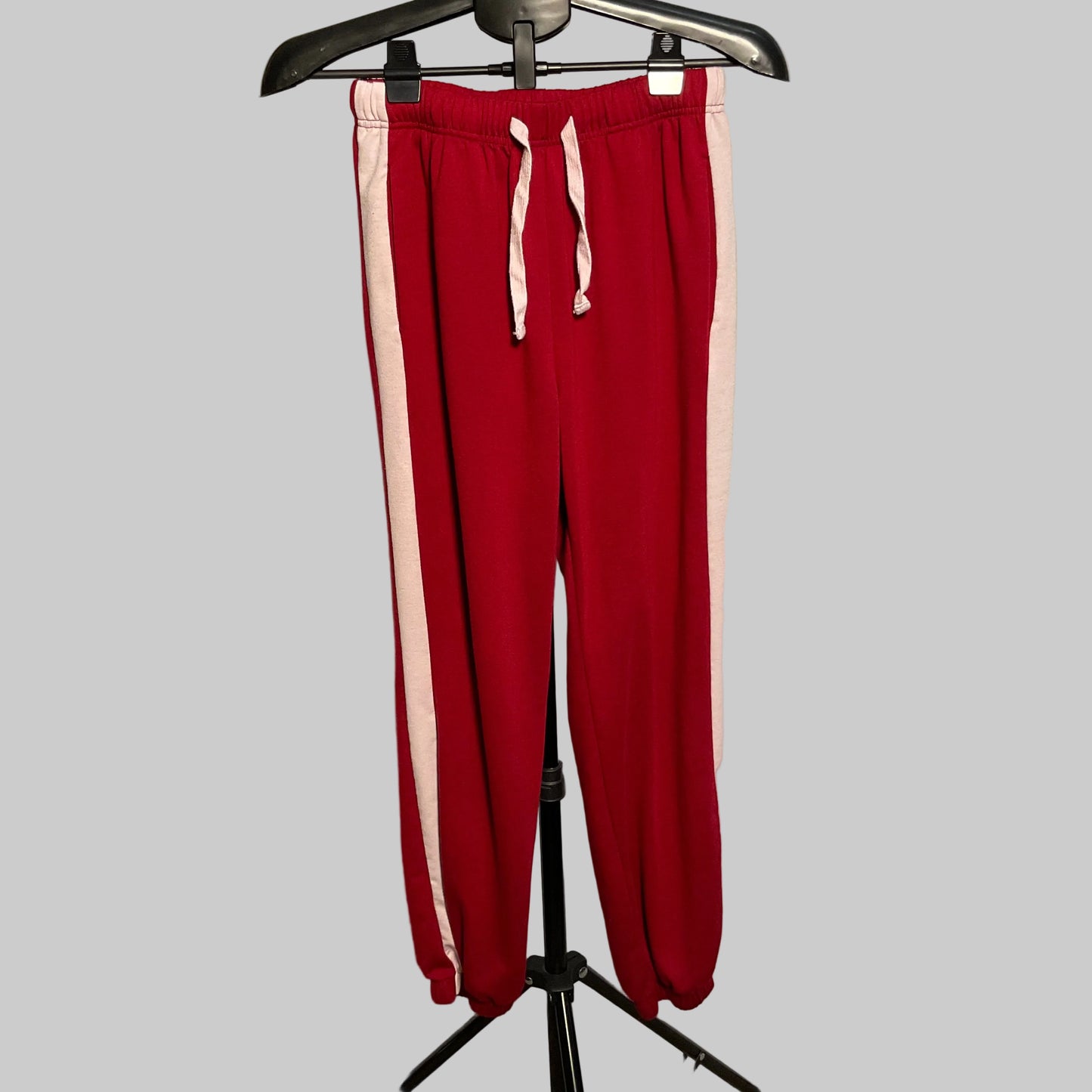 Red jogger sweatpants with white side stripes and white drawstrings, hanging on a black hanger against a white circular backdrop.