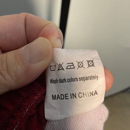A close-up of a hand holding a white fabric care label sewn onto clothing. The label shows washing symbols and the text 'Wash dark colors separately' and 'MADE IN CHINA'.
