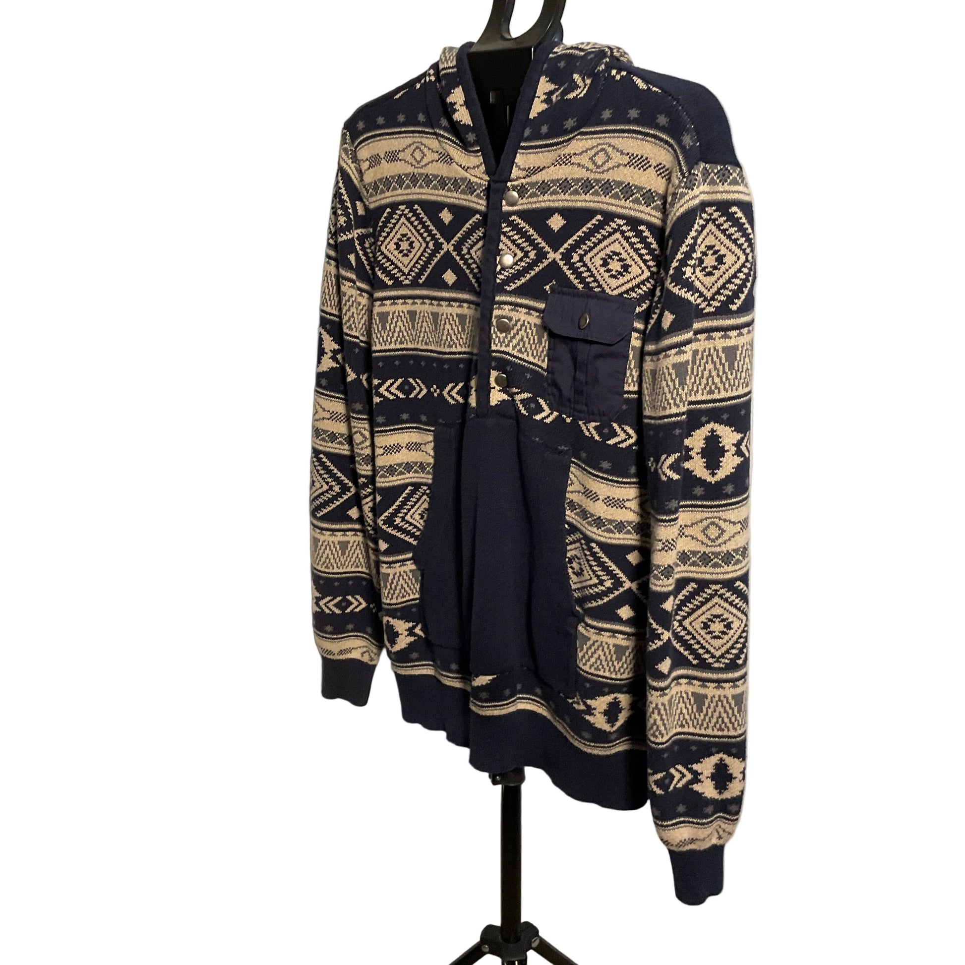 A navy blue and beige patterned zip-up hoodie with a hood and front pockets, displayed on a black hanger stand against a white circular backdrop.