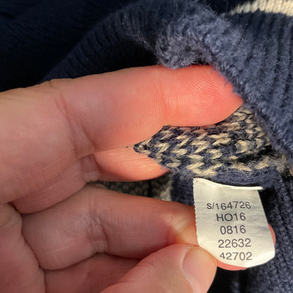 A close-up of a hand holding a small fabric tag sewn onto a navy blue and cream knit garment, showing printed size information.