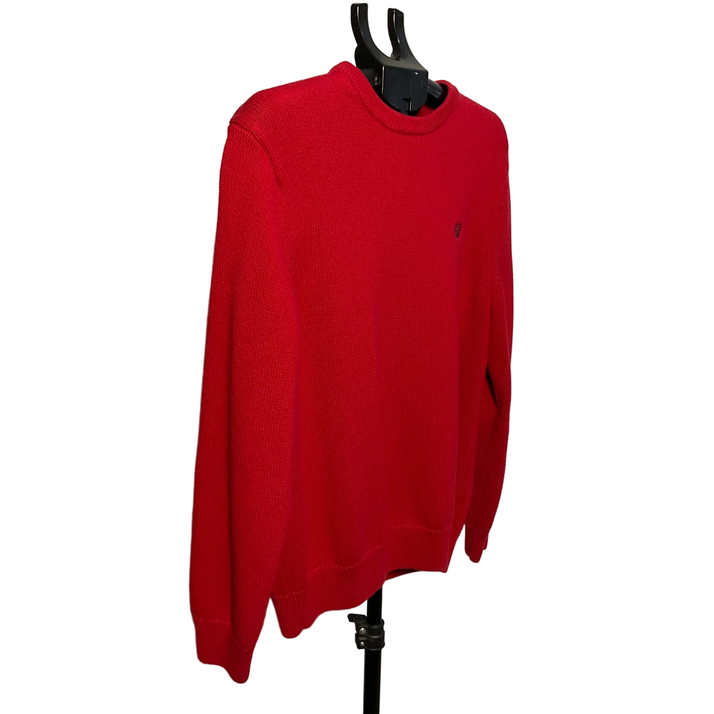 A bright red crewneck sweater hanging on a black hanger stand against a plain off-white wall.