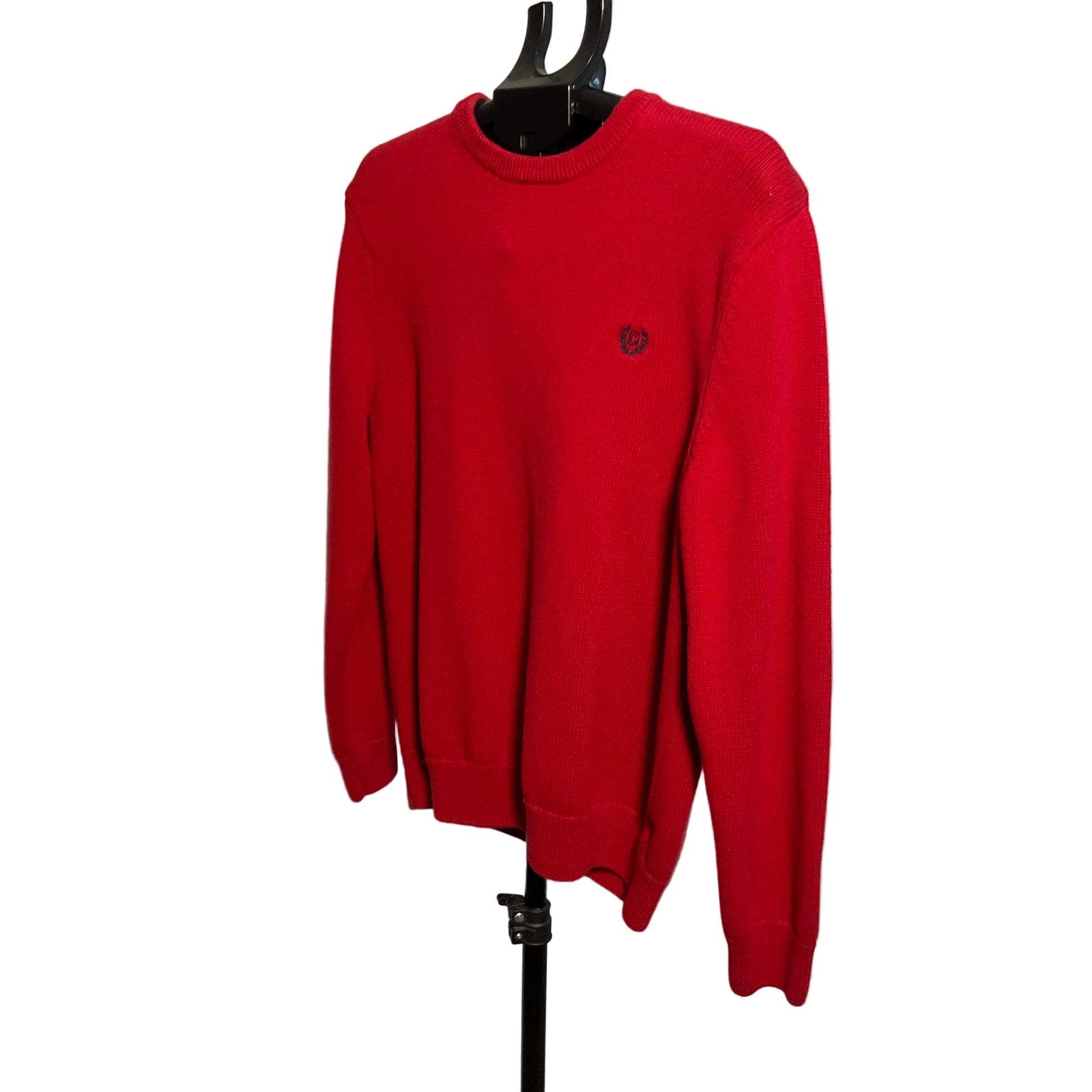 A bright red crewneck sweater displayed on a black hanger against a plain light background. A small embroidered dark logo is visible on the left chest.