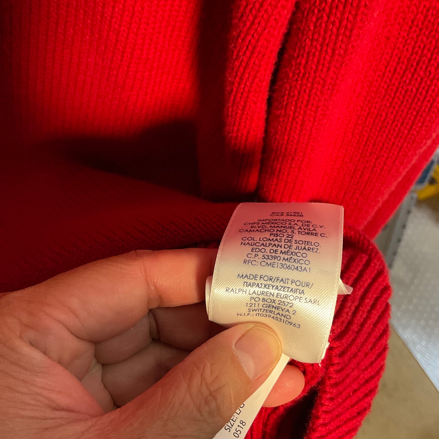 A close-up of a person's hand holding a white product care label attached to a bright red ribbed knit garment.