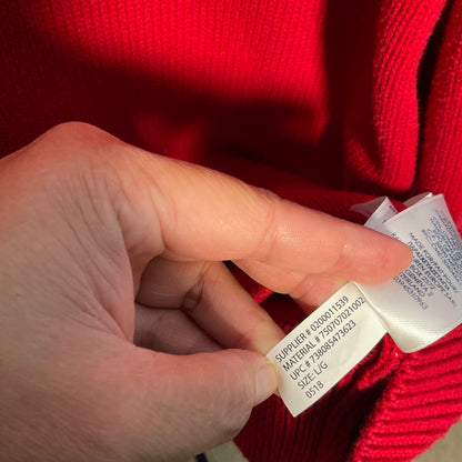 A close-up of a person's hand holding a white fabric care tag next to a red ribbed knit garment.