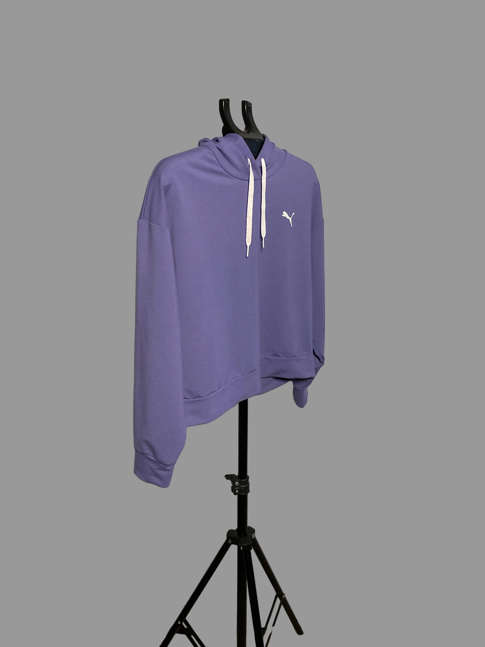 A lavender purple Puma hoodie with white drawstrings and a white cat logo on the chest, displayed on a black hanger stand in front of a circular studio backdrop.