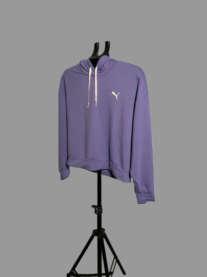 A purple Puma hoodie with white drawstrings and a white cat logo on the chest, displayed on a black hanger stand in front of a circular studio backdrop.