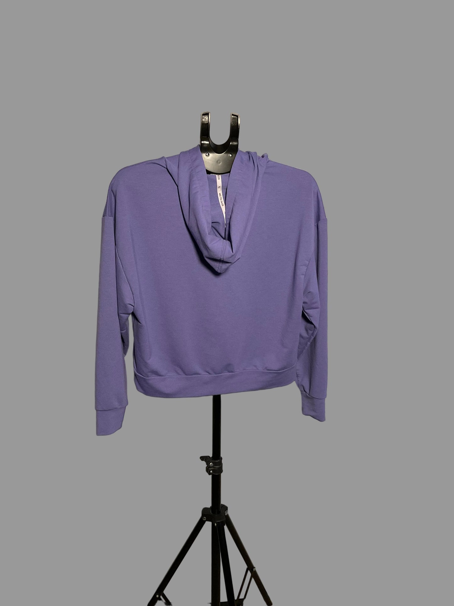 A lavender purple pullover hoodie with a cowl neck and side pockets, displayed on a black hanger stand in front of a circular studio reflector.
