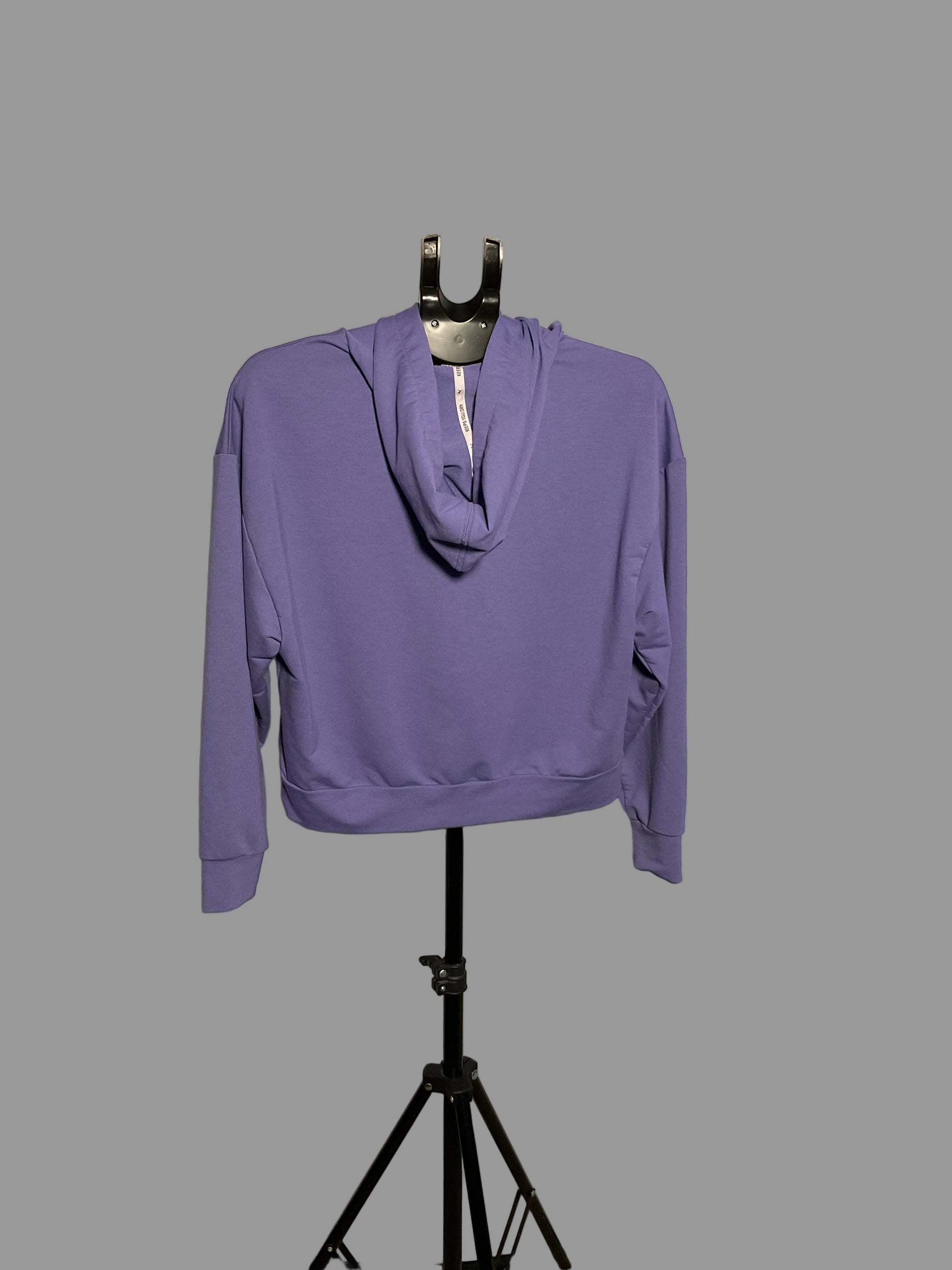A lavender purple pullover hoodie with a cowl neck and side pockets, displayed on a black hanger stand in front of a circular studio reflector.