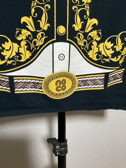 A close-up of a garment on a black stand, featuring a dark navy base with ornate yellow baroque-style scrollwork, a white central panel with a button motif, and a yellow circular patch with the text 'no co'.