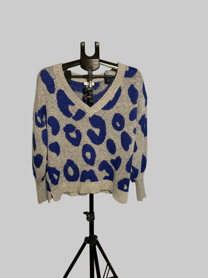A gray knit sweater with a bold blue leopard print pattern, displayed on a black hanger stand in front of a large circular studio reflector.