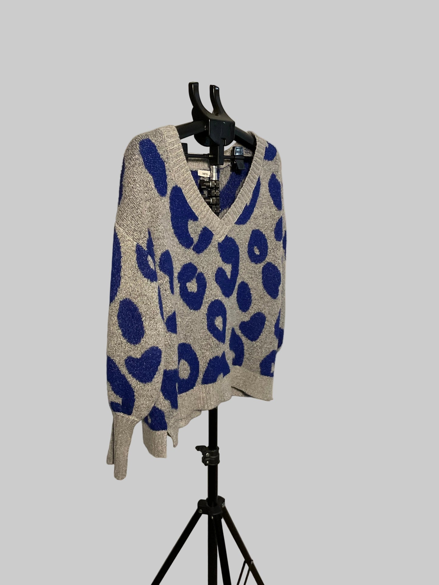 A gray and blue leopard-print knit sweater displayed on a black hanger stand in front of a white studio backdrop.
