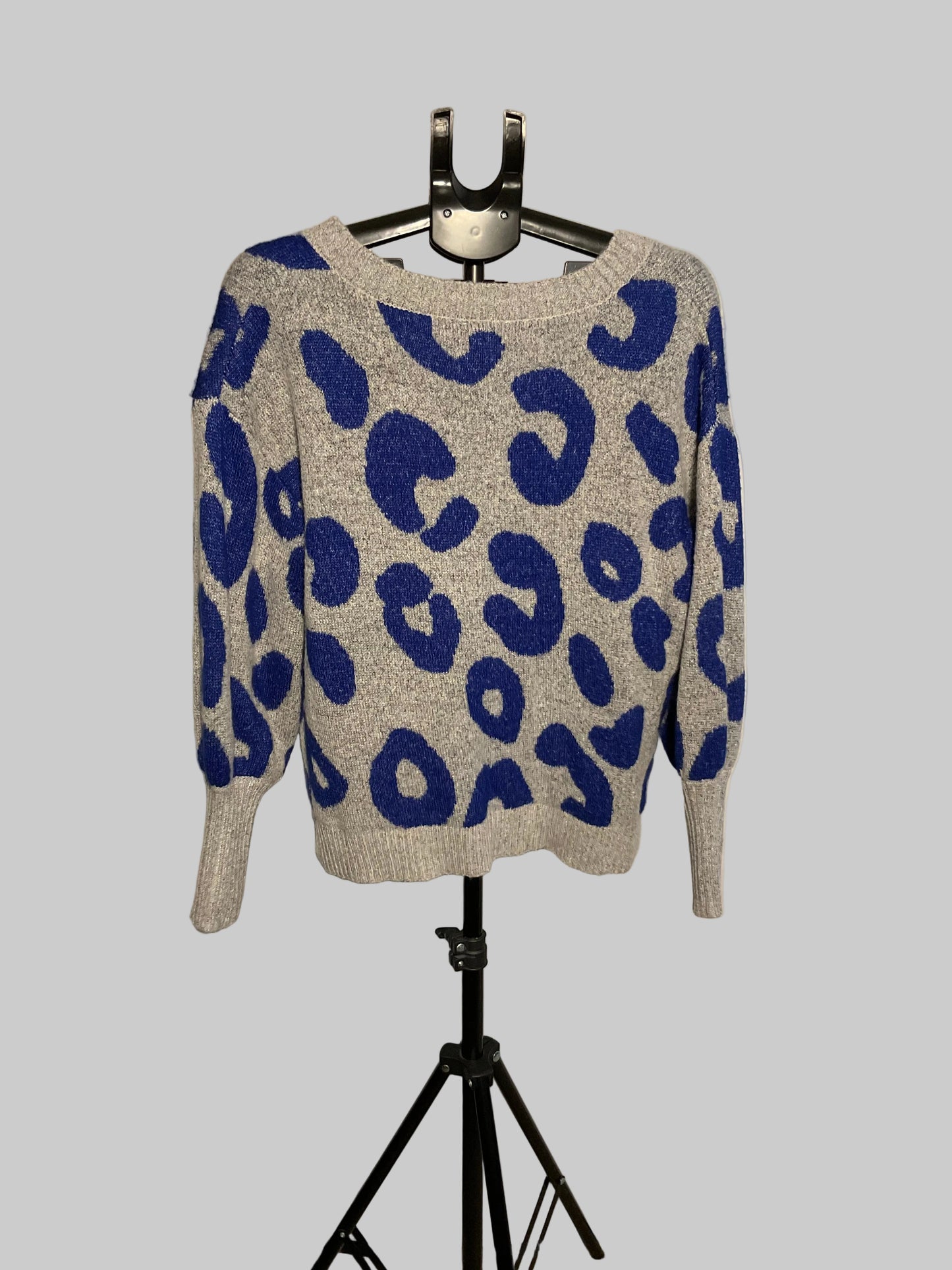 A gray knit sweater with a bold blue leopard print pattern, displayed on a black hanger stand against a white circular studio backdrop.