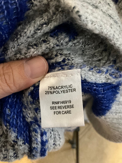 A close-up of a hand holding a white fabric care label sewn onto a chunky knit sweater. The sweater has a heathered gray and bright blue colorway.