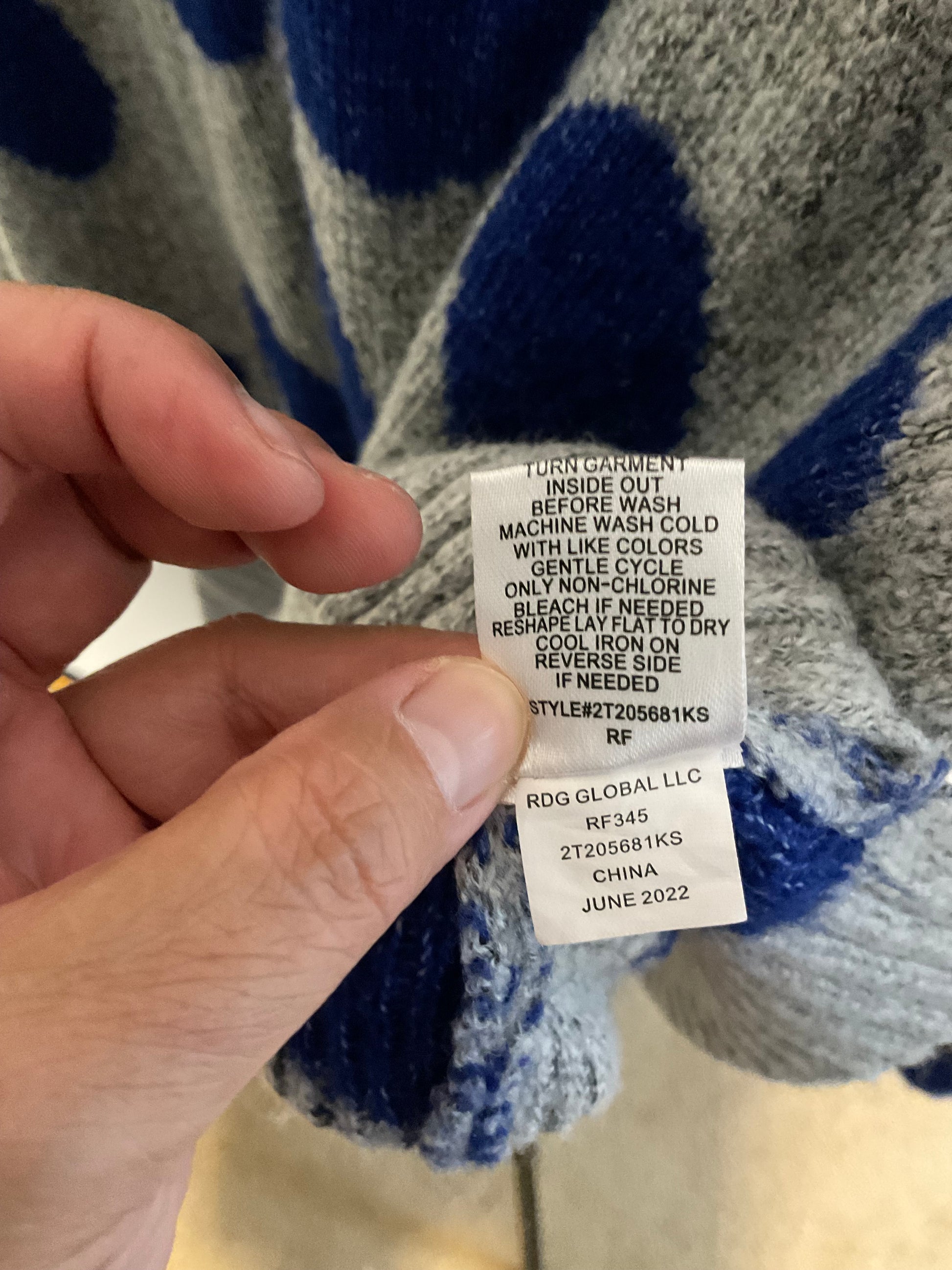 A close-up of a person's hand holding a white product care label sewn onto a fuzzy knit garment with blue and gray polka dots.