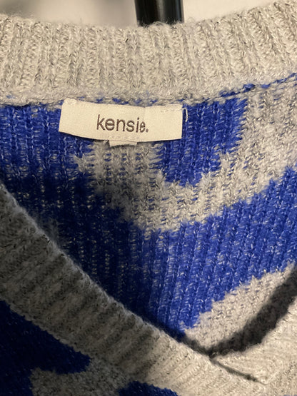 Close-up of a knit sweater showing a cream brand label that reads 'kensie.' The garment has a blue and heather gray patterned knit design.