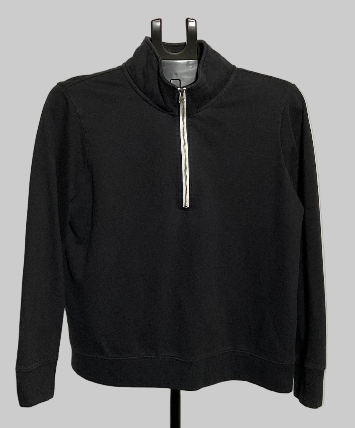 A black long-sleeve quarter-zip pullover sweatshirt displayed on a black hanger stand against a large white circular studio backdrop.