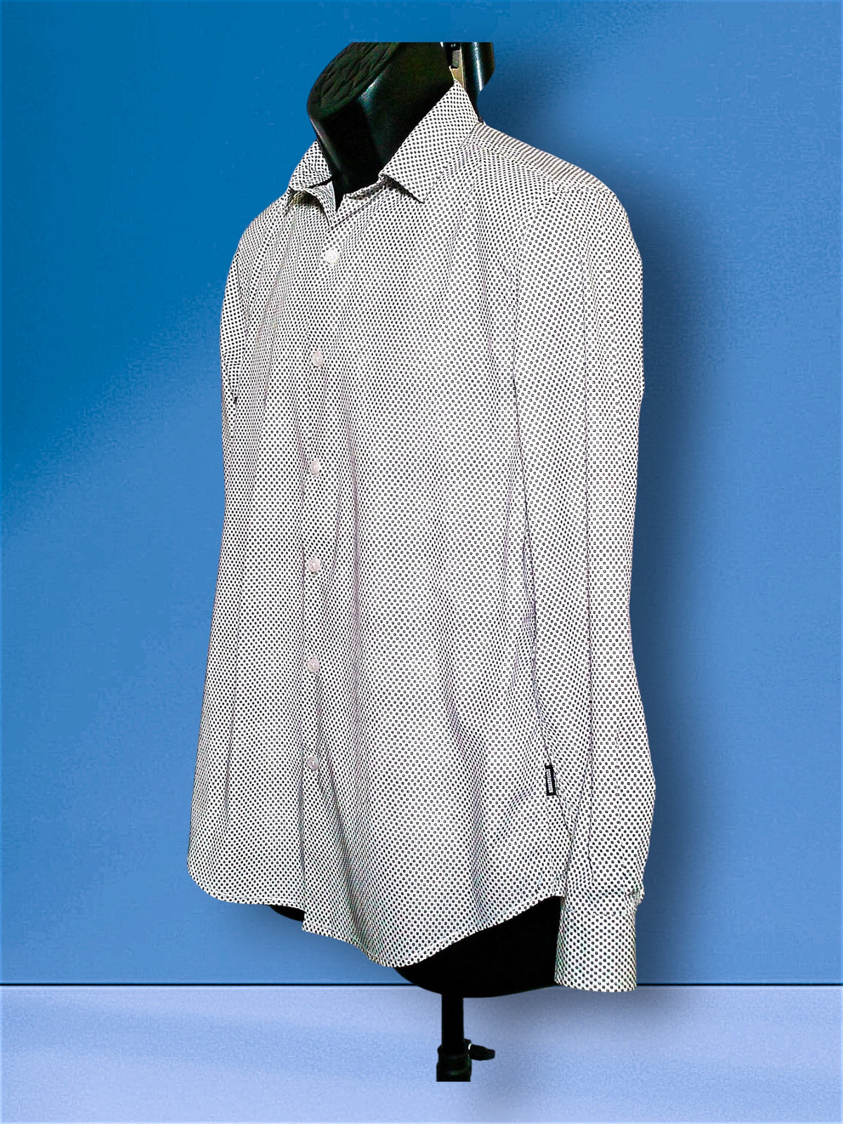 A long-sleeve button-up dress shirt with a small black-on-white micro-dot pattern, displayed on a black mannequin torso against a blue studio background.